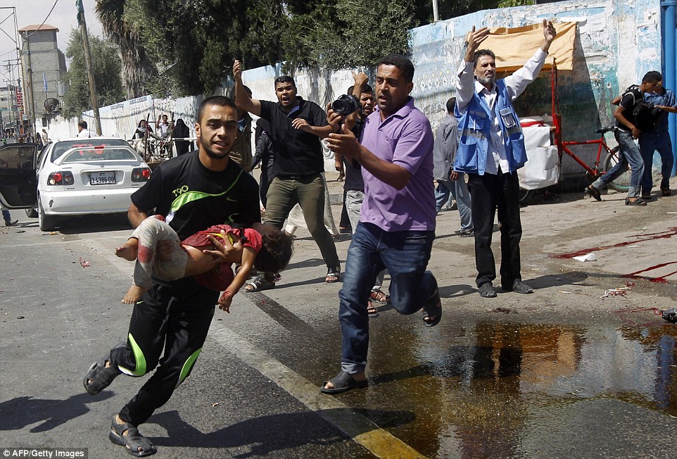 Một người đàn ông bế đứa bé bị thương chạy đi cấp cứu sau khi Israrel oanh kích một trường học của Liên Hiệp Quốc