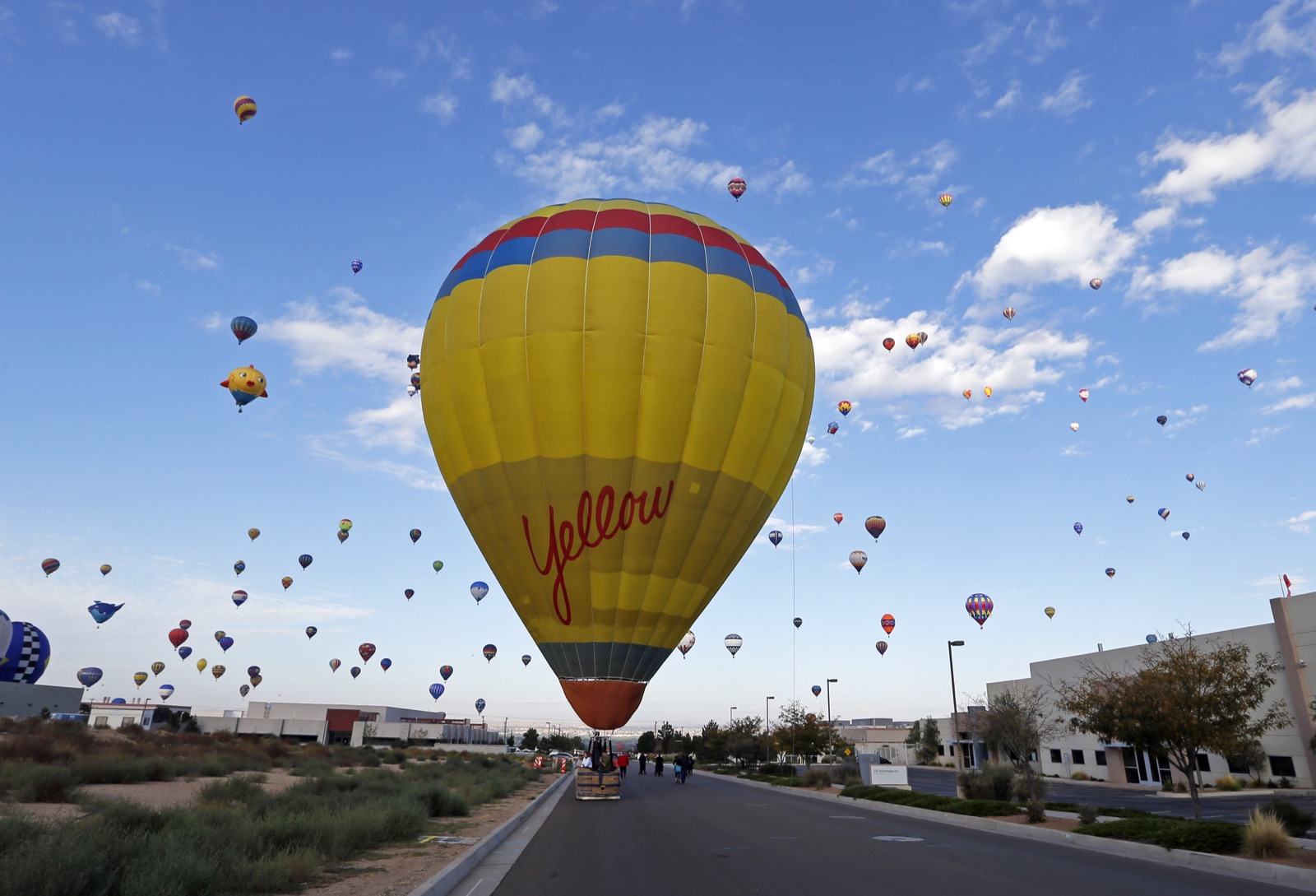 Một chiếc khí cầu được đặt tên là Yellow đang đậu lại bên đường, trong lúc xa xa là hàng trăm khí cầu khác đang bay lơ lửng trên trời. AIBF năm nay là lễ hội khí cầu lần thứ 44 được tổ chức ở Albuquerque, New Mexico. Ảnh chụp bởi Andres Leighton.