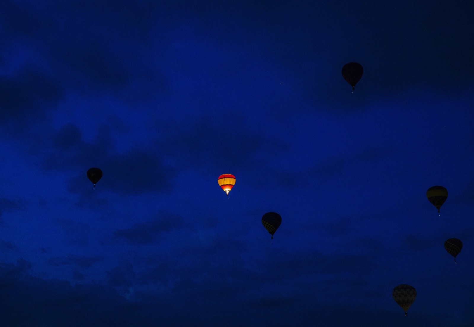Khoảnh khắc chiếc khí cầu được đốt lửa để bay lên, khiến nó phát sáng trong đêm, trong lúc những khí cầu khác tắt lửa nên có màu tối đen. Ảnh chụp bởi Lucas Jackson.