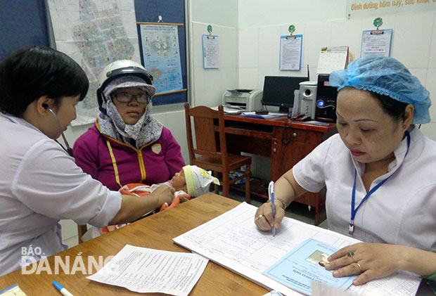 Y sĩ Nguyễn Thị Ngọc Thúy (người bên phải) thực hiện khám sàng lọc và ghi thông tin cho mỗi trẻ nhỏ đến tiêm chủng. Ảnh: Q.T