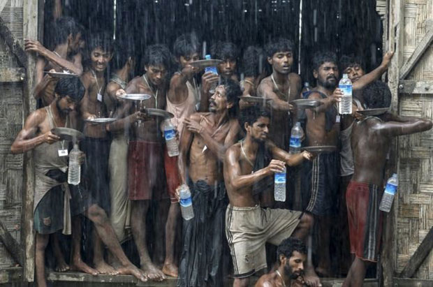 Người di cư ở Myanmar hứng nước mưa. Những người Rohingya và Bangladesh di cư trên đường tới nơi các tổ chức từ thiện đang chờ họ. Họ chen nhau hứng lấy nước mưa bằng chai lọ và dĩa để uống sau khi trải qua nhiều tháng không đủ nước để uống. Ảnh: Soe Zeya 