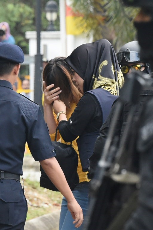 Nghi phạm Đoàn Thị Hương (áo vàng) che mặt khi bị cảnh sát áp giải tới phiên tòa. (Ảnh: AFP)