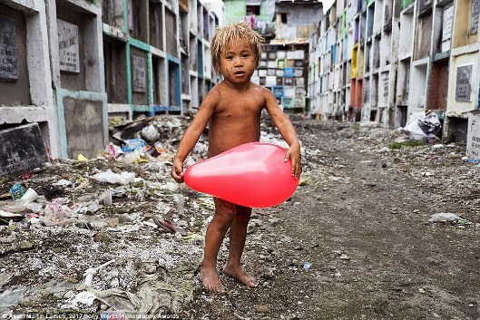 Bức ảnh này được chụp tại một nghĩa trang ở Manila, Philippines, nơi có cộng đồng người vô gia cư sinh sống. Cậu bé này tìm thấy một quả bóng bay để chơi bên cạnh những cái xác vô thừa nhận.