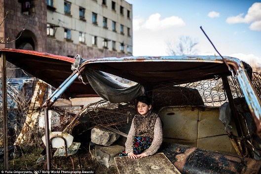 Cô gái chín tuổi tên là Syuzanna ngồi trong vỏ xe ô tô bên ngoài tòa nhà bị bỏ hoang nơi cô sinh sống ở Gymri, Armenia. Tỷ lệ đói nghèo ở đây là 47 phần trăm.