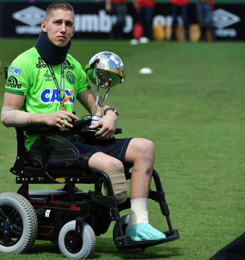 Thủ môn Jackson Follmann đội Chapecoense (Brazil) ngồi trên xe lăn với chiếc chân phải bị cưa sau vụ rơi máy bay tháng 11 năm 2016, tay cầm cúp Copa Sudamericana và được đồng đội đưa ra sân. (Nguồn: baomoi.com)