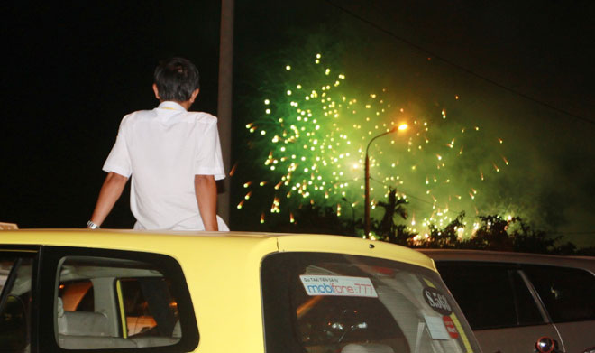 Một du khách xem pháo hoa từ nóc xe taxi. Ảnh: HOÀNG HIỆP