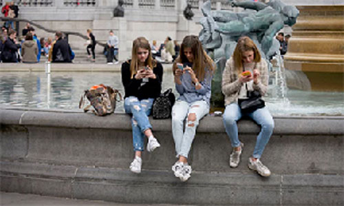 Ba cô gái trẻ trên điện thoại thông minh của họ tại Quảng trường Trafalgar, London.