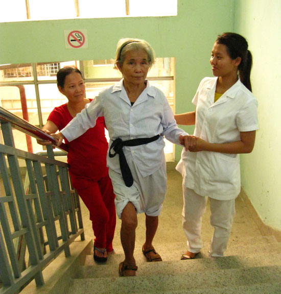 Bà Huỳnh Thị Sừng (giữa) trong vòng tay chăm sóc của con dâu và kỹ thuật viên Bệnh viện Y học cổ truyền Đà Nẵng. Ảnh: V.T.L