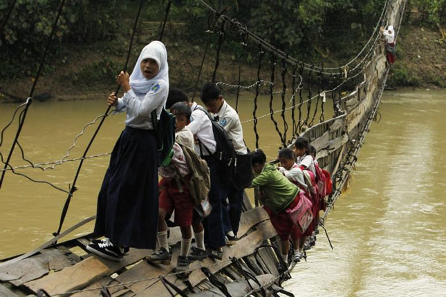 Học sinh bám trên cầu treo bị hư để tới trường ở làng Sanghiang Tanjung (Indonesia).
