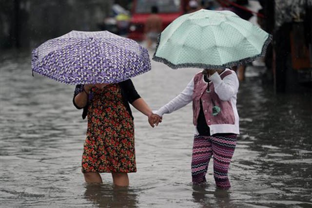 Philippine women hold hands as they ​walk through floodwaters. (Photo: AP/Aaron Favila)