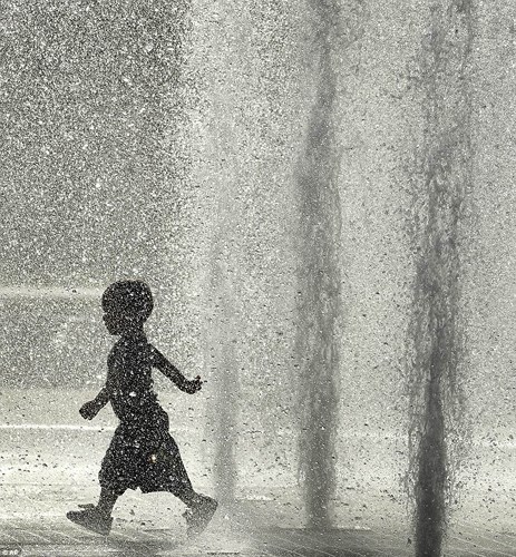 Một đứa trẻ đùa nghịch dưới đài phun nước để tránh nắng nóng ở Kansas. Ảnh: AP