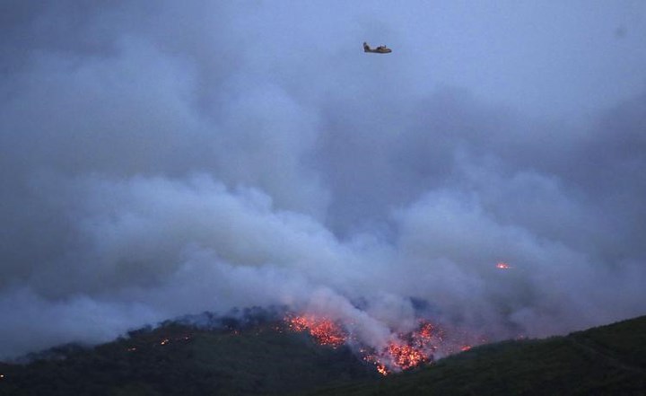   Một chiếc máy bay bay qua thị trấn Mati, phía Đông Athens vào ngày 23/7 khi đám cháy đang bùng lên dữ dội với những cột khói phủ kín không gian. Ảnh: AP