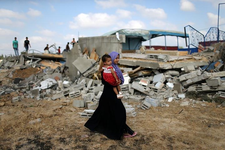 Người phụ nữ Palestine bước qua quang cảnh đổ nát tan hoang sau vụ không kích của Israel.