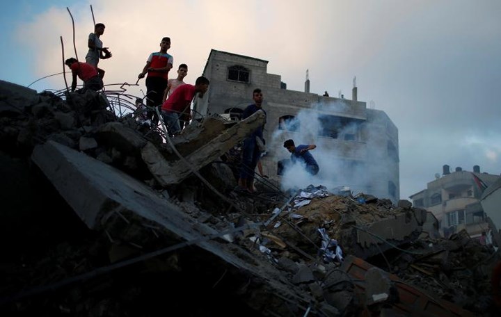 Những người dân Palestine thu dọn đống đổ nát của một tòa nhà bị trúng bom của Israel.