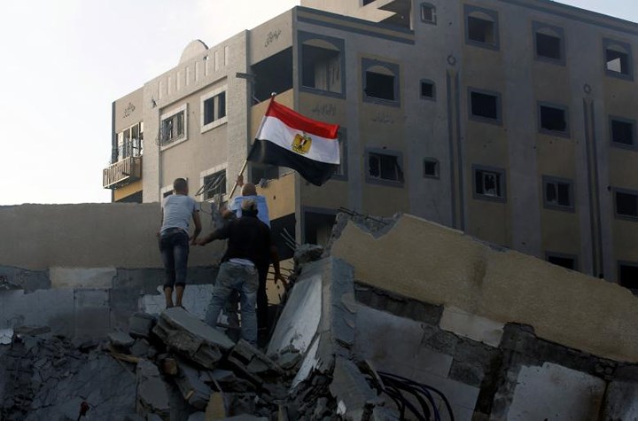 Một người đàn ông Palestine cắm cờ của Ai Cập lên đống đổ nát của một tòa nhà sau cuộc không kích của Israel.