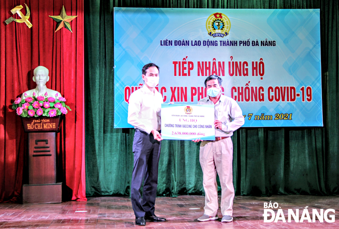 Chủ tịch Liên đoàn Lao động thành phố Nguyễn Duy Minh (bên trái) trao bảng tượng trưng ủng hộ chương trình vắc-xin cho công nhân thông qua Quỹ xã hội từ thiện Tấm lòng vàng Báo Lao động.  Ảnh: XUÂN HẬU	