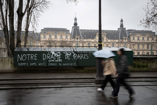 Hai người đi bộ đang bước qua phía trước một tiệm sách đã đóng cửa nằm ở bờ bên trái của sông Seine tại Paris, Pháp. (Ảnh chụp ngày 7-2-2024)Ảnh: AFP