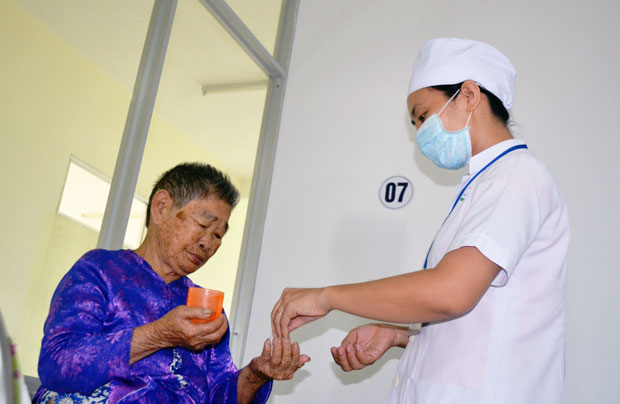 Bà Phan Thị Sương (72 tuổi) được nhân viên điều dưỡng hỗ trợ việc uống thuốc tại khoa Lão, Trung tâm Y tế quận Ngũ Hành Sơn. 