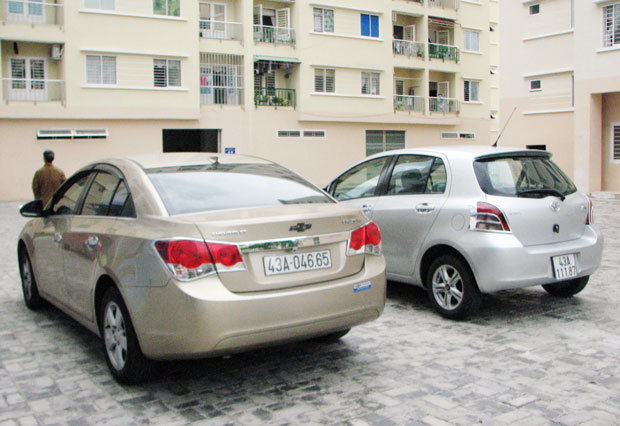 Chiếc ô-tô (trái) đậu trong khu vực dãy nhà chung cư Vicoland bị kẻ gian cạy cả logo trước lẫn sau.
