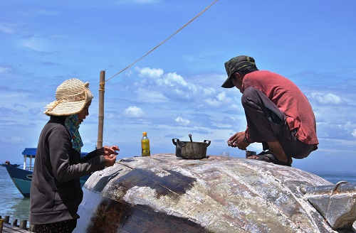   Under the blazing sun, two local fisherfolk use dipterocarpus wood resin to  waterproof their coracle