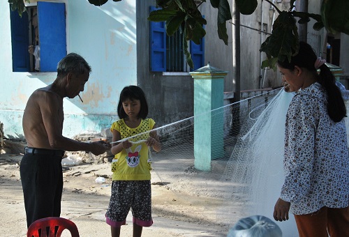   An elderly fisherman teaching his granddaughter how to weave a fishing net