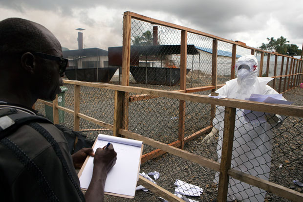 Một nhân viên y tế đưa cho đồng nghiệp thông tin người bệnh vào cuối ca trực tại trung tâm điều trị Ebola ở Monrovia (Liberia).  				                        Ảnh: Reuters