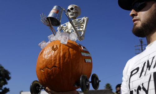 Một người đàn ông cầm chiếc lồng đèn bí ngô Jack-O Lantern, ngồi trên là một bộ xương cầm chiếc xô của thử thách dội nước đá (Ice Bucket Challenge) trong cuộc đua bí ngô Halloween ở biển Manhattan, bang California, Mỹ.