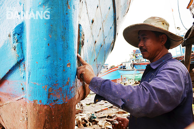 Thợ Phạm Hải đang dùng xơ tre, keo dán để bịt các kẽ nứt trên thân tàu.