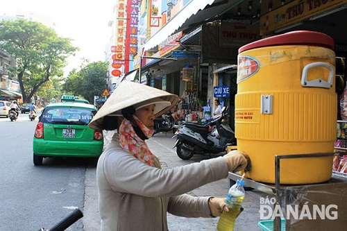  A local woman taking free iced tea from a barrel put on the street’s pavement