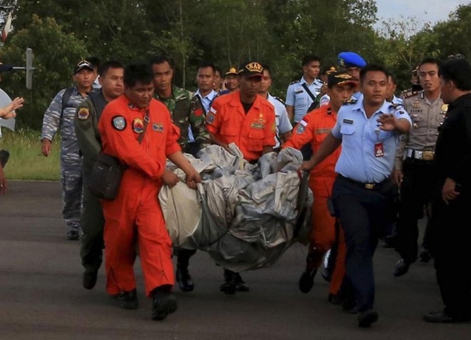 Các nhân viên áo cam vừa vớt bộ phận máy bay của AirAsia lên bờ. Ảnh: Reuters