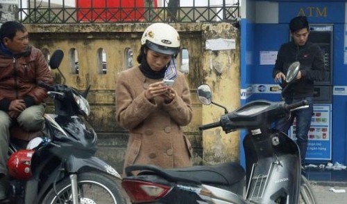 A woman (C) types on a mobile phone along a street in Hanoi February 2, 2015. Reuters