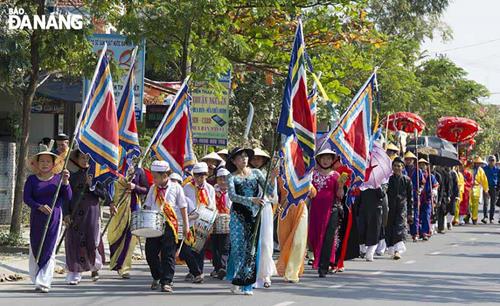 Local pupils beat drums whilst local women in ao dai carry festive flags.