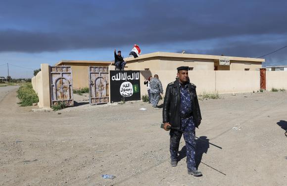 An Iraqi officer walks past a wall painted with the black flag commonly used by Islamic State militants, in the town of Tal Ksaiba, near the town of al-Alam, March 7, 2015. 