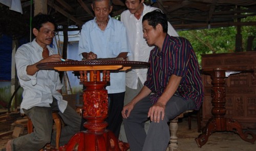 Dinh Tham (L, 2nd) and two skillful carpenters, Pham Mien (L, 3rd) and Tran Ngoc Tuan (R), are seen checking the decorations of a self-turning table in Van Ha Village.