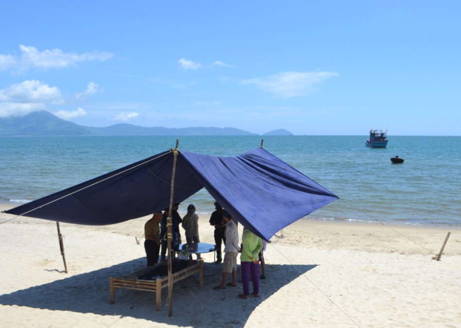 Thi thể người quá cố được chuyển lên bờ, ngoài xa là tàu cá đưa thi thể này từ biển về đất liền