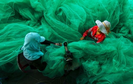 Bức “Đan lưới” của nhiếp ảnh gia Phạm Tỵ chụp ở vịnh Vĩnh Hy (Ninh Thuận), ghi lại cảnh hai người phụ nữ đang cần mẫn ngồi đan lưới, những tấm lưới gợn sóng như thể sóng biển đang bủa vây xung quanh họ.