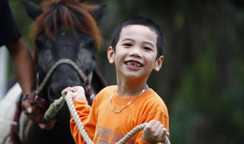 A child smiles while taking a horse for a walk at the Hanoi Horse Club in Cau Giay District. Simple activities like taking horses for a walk, feeding or fondling them help children become more confident. Tuoi Tre