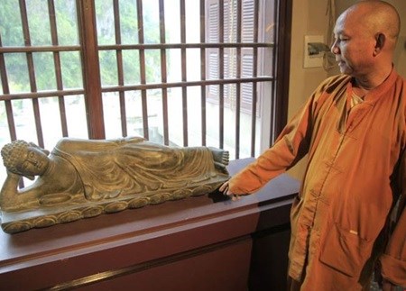 Reclining Buddha: Thich Hue Vinh, the abbot of Quan The Am Temple introducing a valuable antique which has been stored in his temple for a long time. (Source: thanhnien.vn)