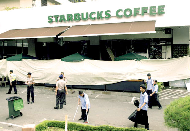 Các nhân viên dọn dẹp bên ngoài quán cà-phê Starbucks, một trong những nơi xảy ra vụ tấn công khủng bố. An ninh được thắt chặt trên khắp Indonesia. 									                     Ảnh: AP