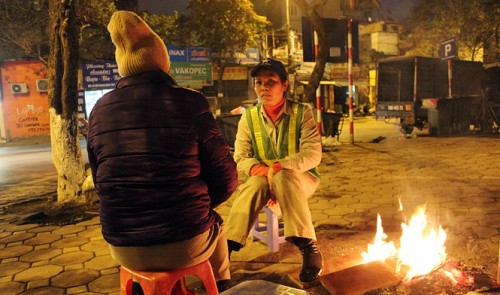 Two people warm themselves up beside a fire in Ha Noi.