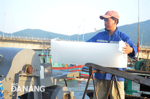 A fisherman placing an ice bar into an ice crusher machine