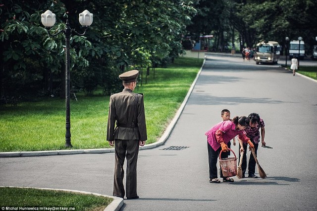 Hai người lao công đang quét dọn tại một công viên ở Bình Nhưỡng dưới sự giám sát của một người lính