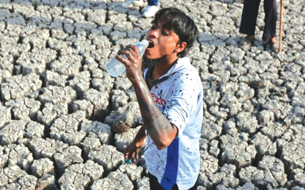 Người đàn ông Ấn Độ đang tạm nghỉ tay uống nước trong lúc nhặt cá chết ở hồ Vastrapur đã trơ đáy từ tháng trước.
