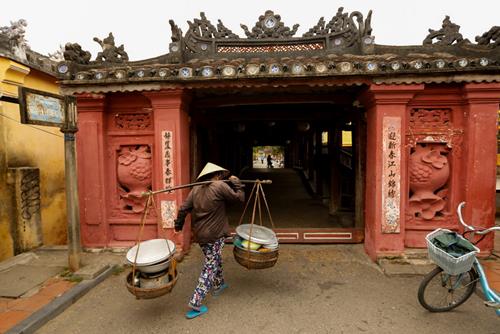 A woman wearing a traditional hat, known as a non la, sells breakfast at the Japanese Bridge in Hoi An, Vietnam April 5, 2016. Photo: Reuters