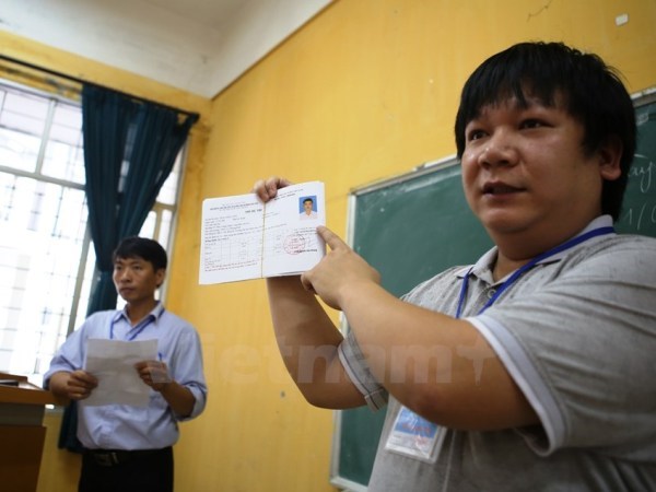 Cán bộ coi thi hướng dẫn thí sinh làm thủ tục dự thi trung học phổ thông quốc gia. (Ảnh: Vietnam+)