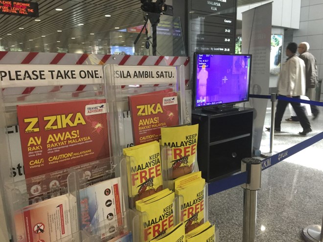 Travellers walk past travel advisory on the Zika virus infection and a body temperature scanner in Kuala Lumpur International Airport (KLIA) on Aug 28, 2016 (Photo: AP)