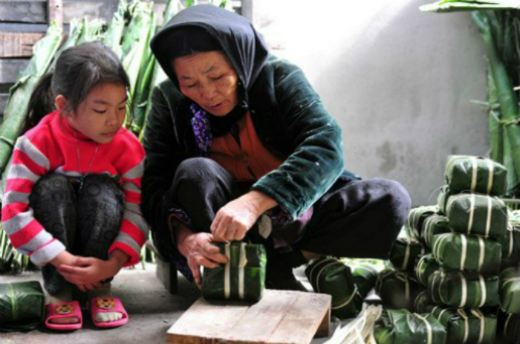 A woman in Hanoi shows her grandchildren how to wrap a banh chung. Photo by VnExpress/Hoang Ha