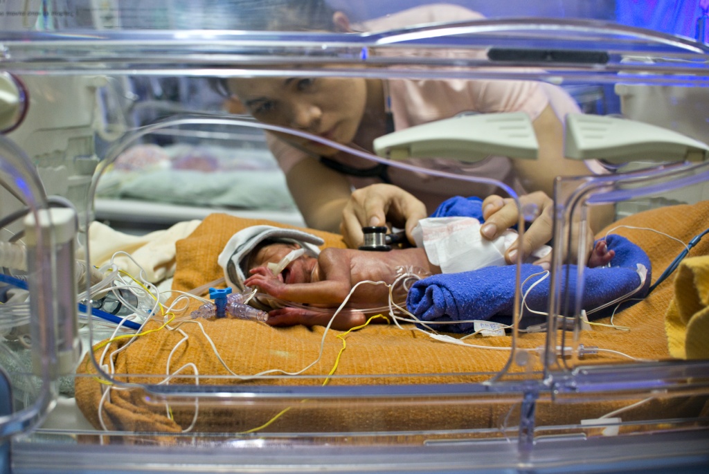 A nurse examines a baby in an incubator.