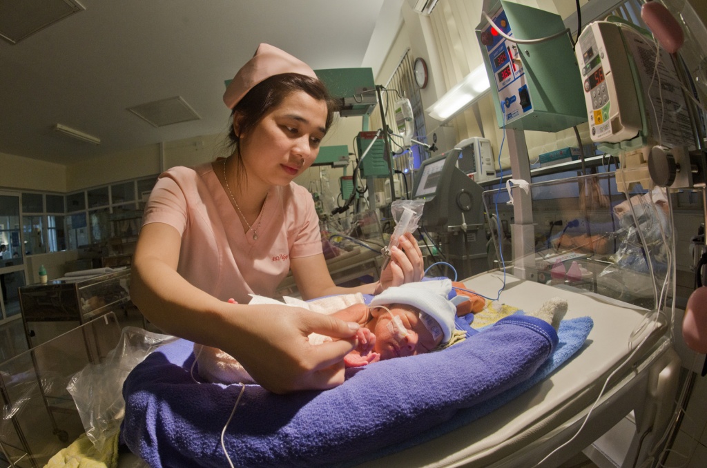 A baby sleeps while holding a nurse’s finger.