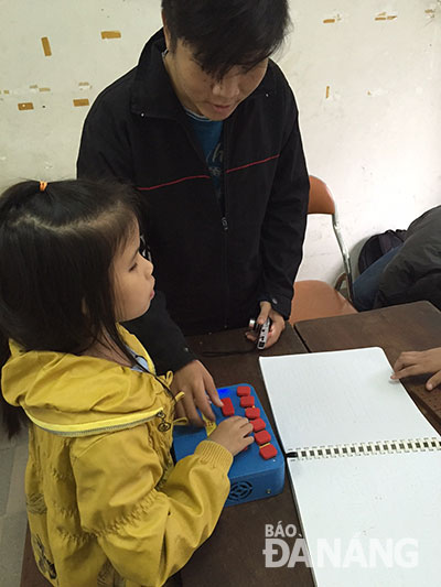 Hoai Linh showing a blind girl how to use a Braille keyboard